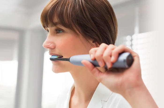 En kvinde børster tænder med en grå Philips Sonicare.