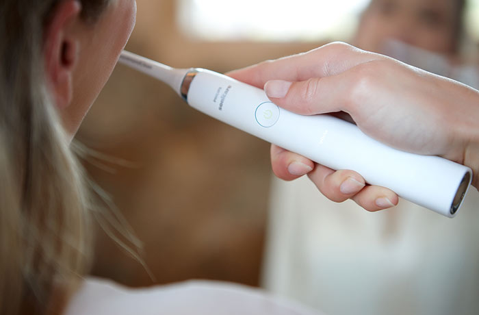Nærbillede af en kvinde, der børster sine tænder med en hvid Sonicare-eltandbørste fra Philips.