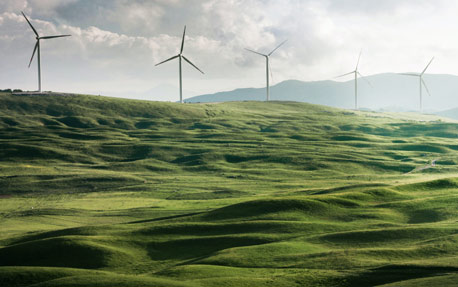 Et billede af en gr&oslash;n skr&aring;ning med roterende vindm&oslash;ller, der genererer vedvarende energi, i baggrunden.